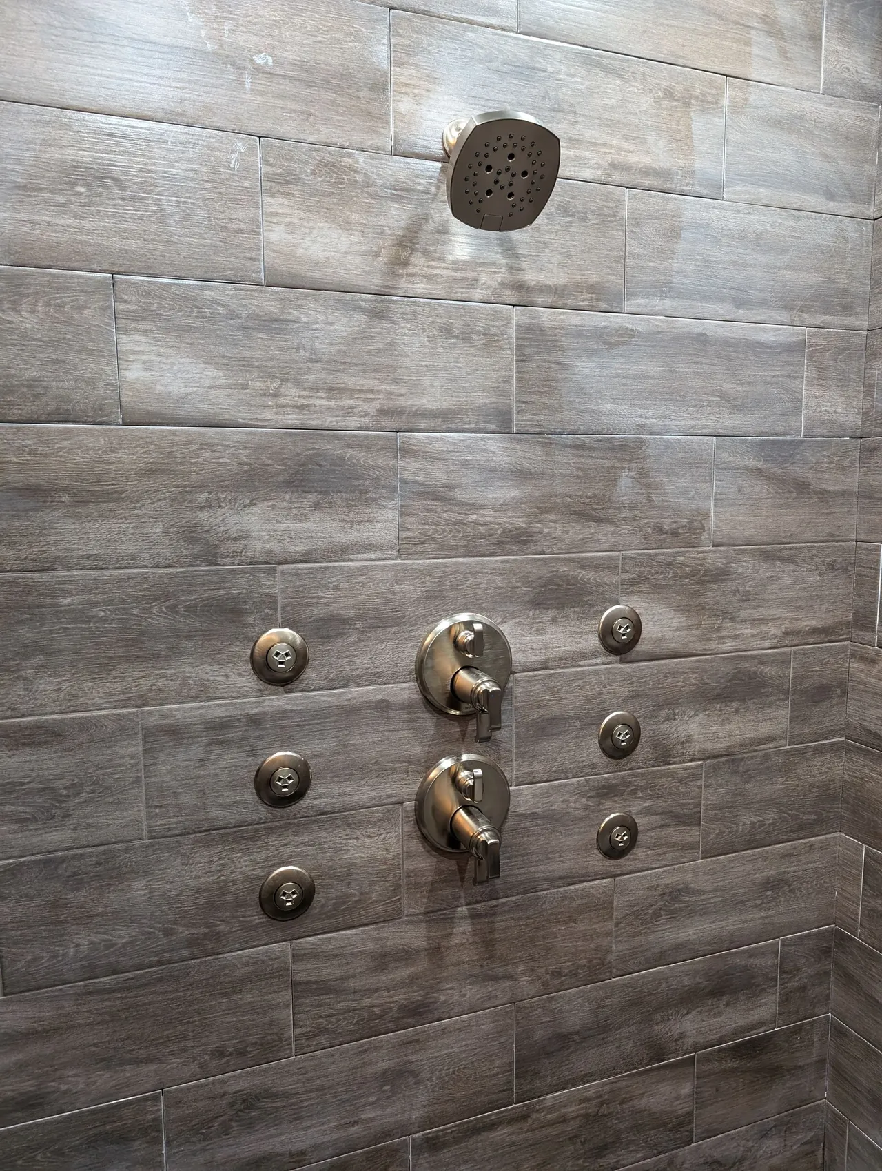 Dark tiled shower wall with metal knobs and a circular showerhead opening