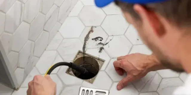 Plumber inspecting a wall pipe leak in a white tiled shower corner